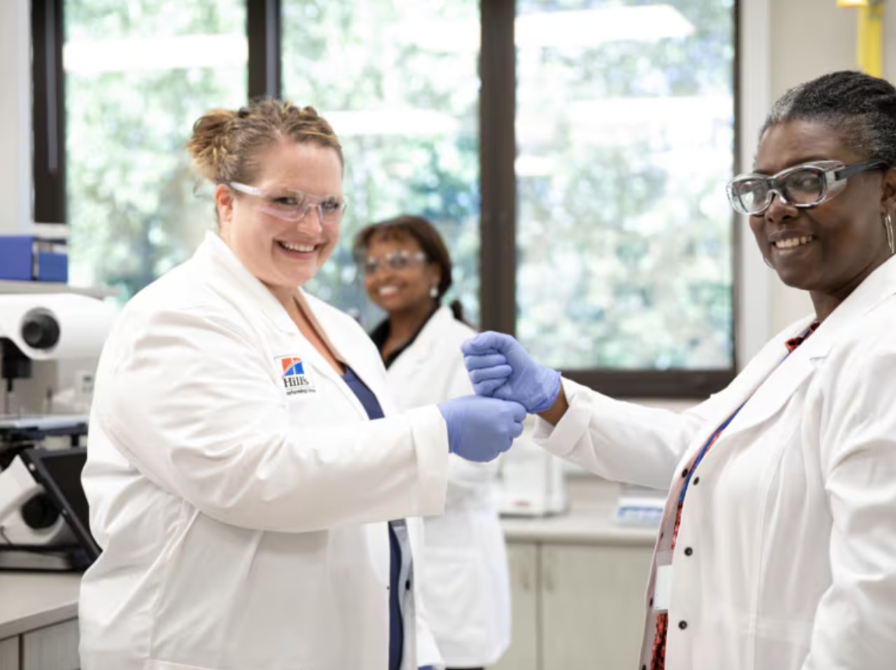 tres mujeres sonrientes, científicas con batas blancas y gafas protectoras